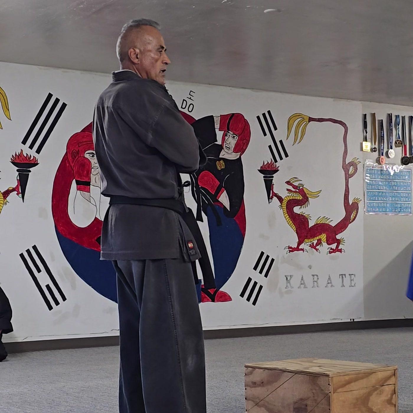 Mundo Chavez, 5th Dan in Tang Soo Do, in his dobok in front of the dojo mural during class