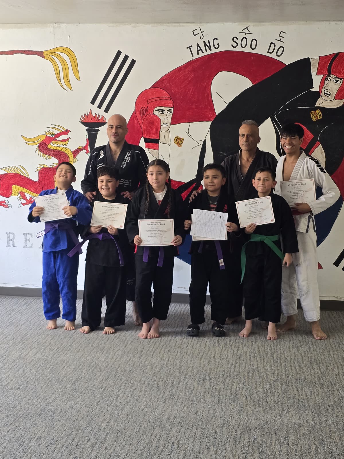 Belt test day — students with their certificates in front of the Tang Soo Do mural