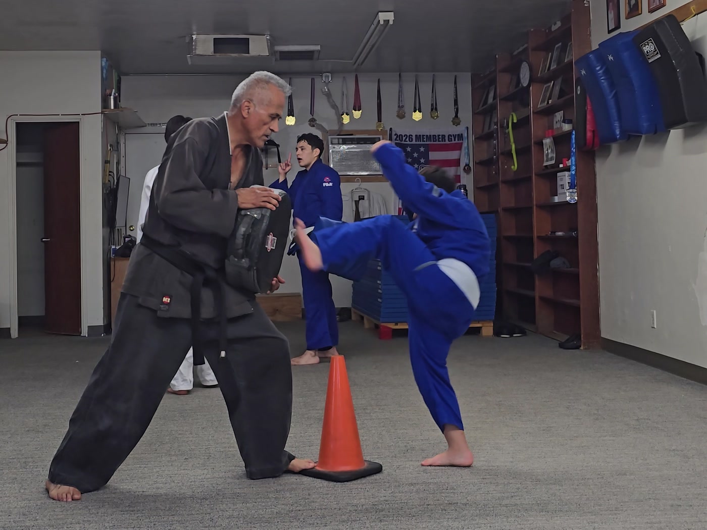 Young student in a blue gi kicking the pad held by instructor Mundo.