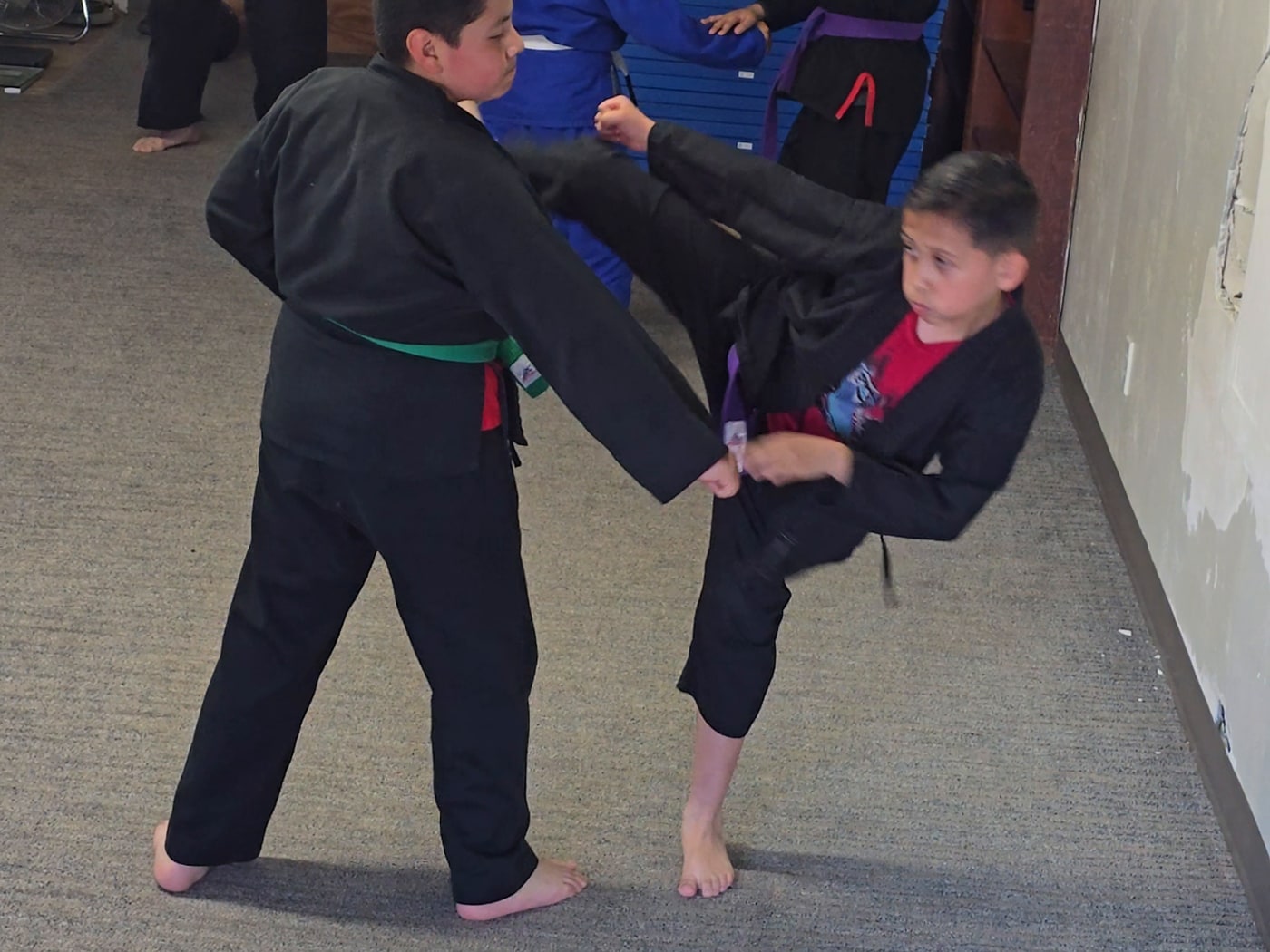 Youth student in a purple belt landing a side kick on a sparring partner.